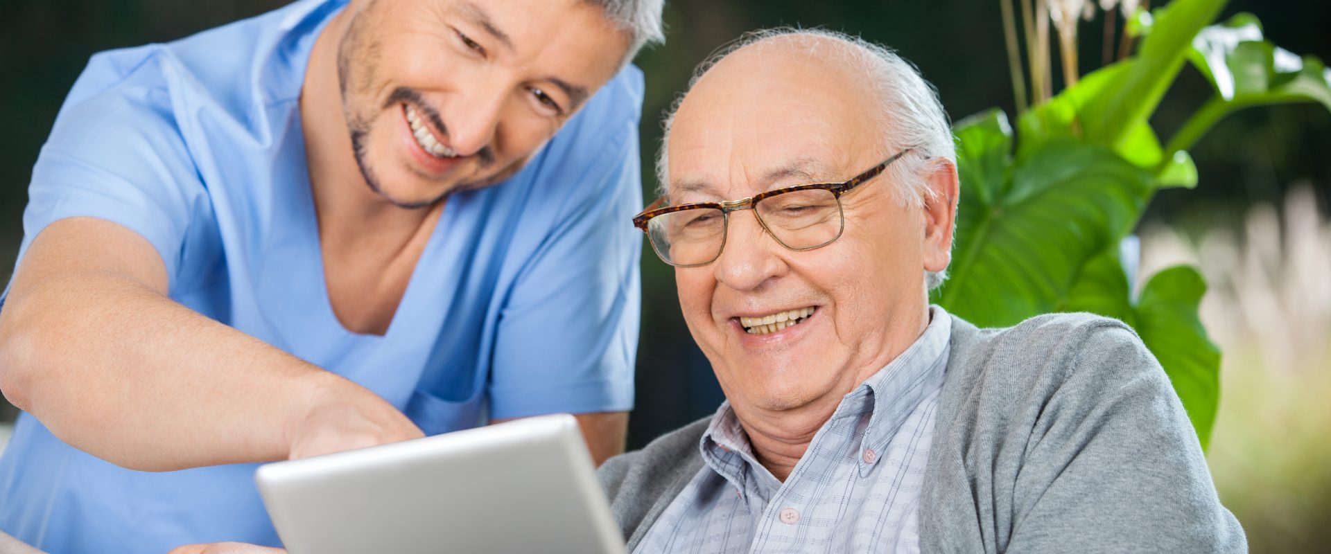 Happy male nurse and senior man enjoying while using tablet computer in nursing home porch